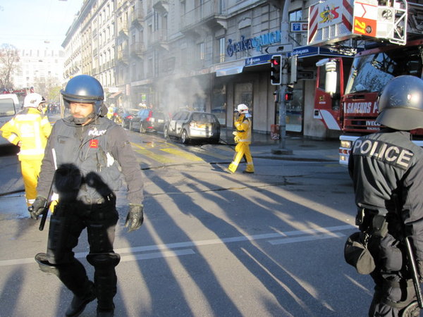 Police direct WTO marchers away from a burnt-out car in Geneva yesterday.