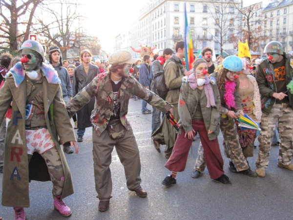 A group of clowns dressed in army gear mimics police a few metres away, holding the line #WTO #Geneva